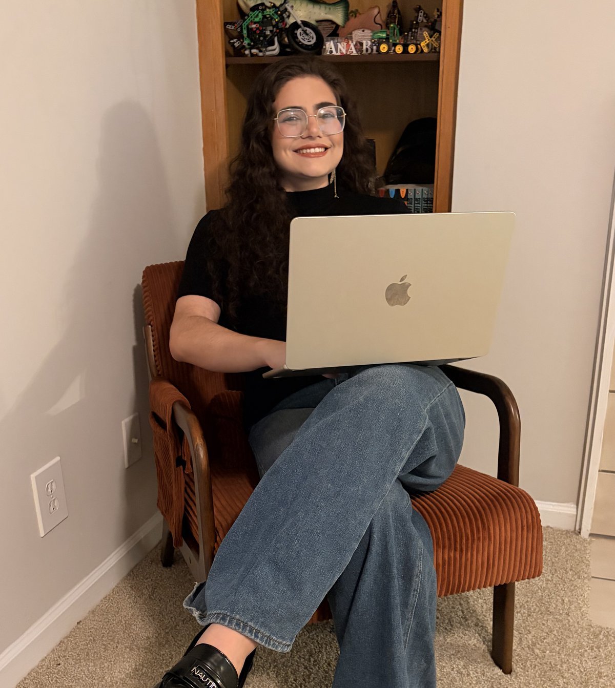 Ana Tereza Netto Viana sorrindo, sentada em uma poltrona com o notebook no colo